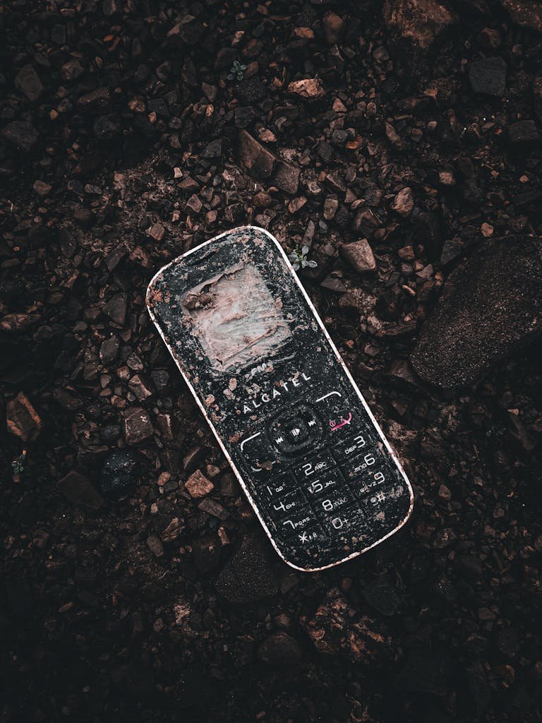 A weathered cellphone lies on rocky ground, showcasing urban decay in Albania.