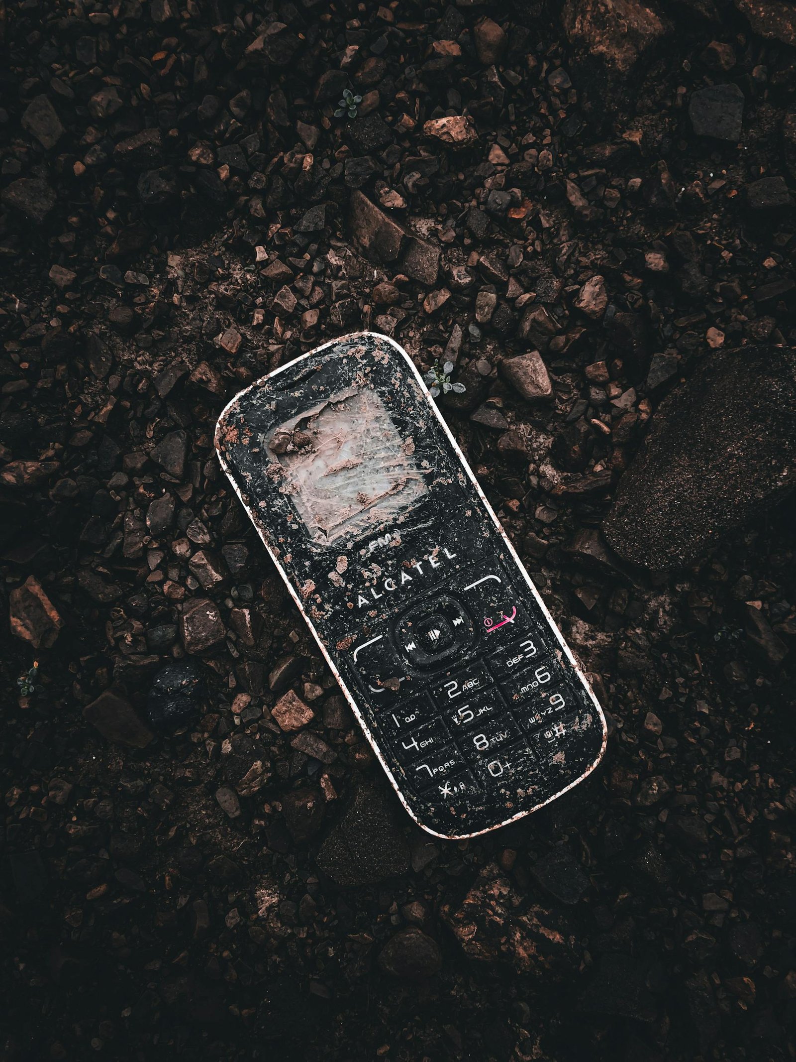 A weathered cellphone lies on rocky ground, showcasing urban decay in Albania.