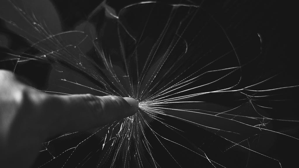 Black and white close-up of a finger touching a cracked glass screen, creating a dramatic effect.